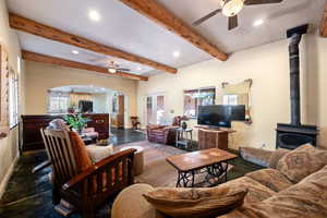 Living room with recessed lighting, arched walkways, a ceiling fan, beamed ceiling, and a wood stove