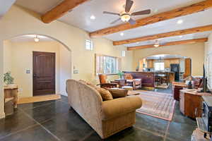 Living room featuring arched walkways, beamed ceiling, recessed lighting, ceiling fan, and concrete flooring