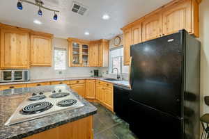 Kitchen featuring black appliances, glass insert cabinets, recessed lighting, light brown cabinets, and a textured ceiling