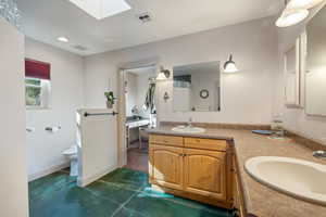 Bathroom with a skylight, double vanity, recessed lighting, and dark tile patterned floors