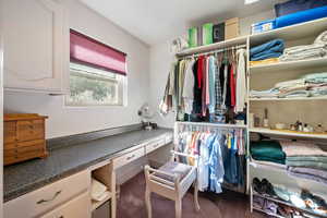 Spacious closet featuring built in desk and dark carpet