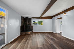 Unfurnished living room with a textured ceiling, dark wood-type flooring, beam ceiling, and a wood stove