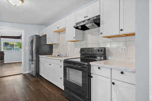 Kitchen with black range with electric cooktop, tasteful backsplash, under cabinet range hood, white cabinetry, and a textured ceiling