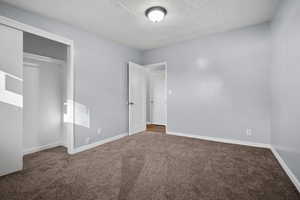 Unfurnished bedroom with a textured ceiling, carpet floors, and a closet