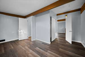 Unfurnished room featuring a textured ceiling, dark wood-style floors, and beamed ceiling