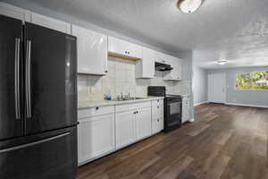 Kitchen with black appliances, light countertops, white cabinetry, decorative backsplash, and dark wood-style floors