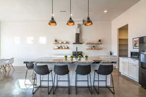 Kitchen with concrete flooring, light stone countertops, a kitchen island with sink, white cabinets, and recessed lighting