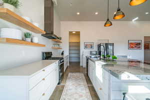 Kitchen with white cabinetry, stainless steel gas range oven, open shelves, finished concrete floors, and wall chimney range hood