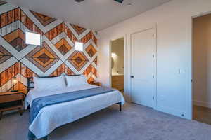 Carpeted bedroom with an accent wall, a ceiling fan, and ensuite bath
