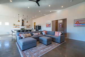 Living room featuring concrete flooring, a ceiling fan, recessed lighting, and a towering ceiling