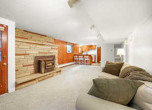 Carpeted living room featuring wood walls, a wood stove, and baseboard heating