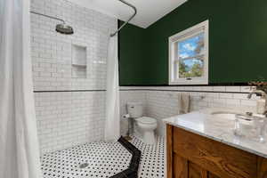Full bath with tile walls, vanity, a shower stall, wainscoting, and tile patterned flooring