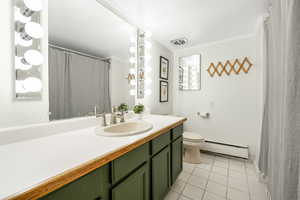 Full bath featuring light tile patterned flooring, vanity, curtained shower, baseboard heating, and crown molding