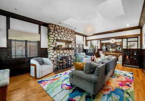 Living area with a skylight, light wood finished floors, a stone fireplace, and a wainscoted wall