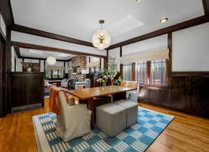 Dining space with a skylight, wood finished floors, a wainscoted wall, beam ceiling, and a chandelier