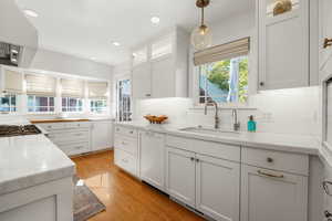 Kitchen featuring glass insert cabinets, white cabinetry, premium range hood, light stone counters, and recessed lighting