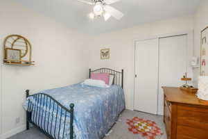 Carpeted bedroom with ceiling fan and a closet
