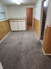 Kitchen with wooden walls, white cabinets, light colored carpet, wainscoting, and light countertops