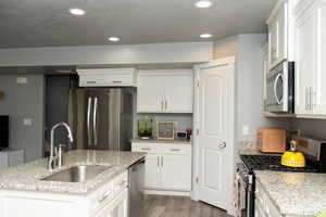 Kitchen with appliances with stainless steel finishes, light wood-type flooring, light stone counters, white cabinets, and recessed lighting