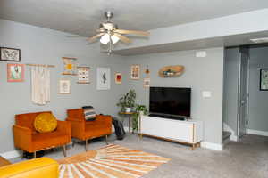 Carpeted living area featuring ceiling fan and baseboards
