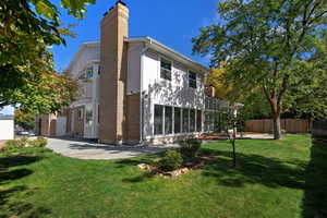 Rear view of property featuring a chimney, brick siding, stucco siding, and a sunroom