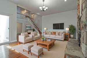 Living room with wood finished floors, stairway, a stone fireplace, a chandelier, and a high ceiling