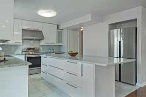 Kitchen with appliances with stainless steel finishes, light stone counters, exhaust hood, decorative backsplash, and a center island