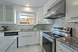 Kitchen with electric range, under cabinet range hood, white cabinets, and light stone counters