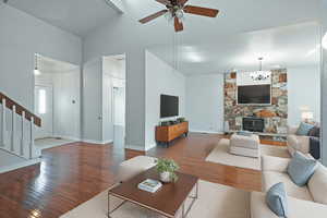 Living room featuring wood-type flooring, a chandelier, a stone fireplace, a ceiling fan, and stairs