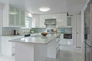 Kitchen featuring glass insert cabinets, light stone countertops, stainless steel appliances, extractor fan, and white cabinetry