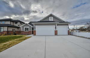 Craftsman-style home with concrete driveway, an attached garage, board and batten siding, roof with shingles, and brick siding