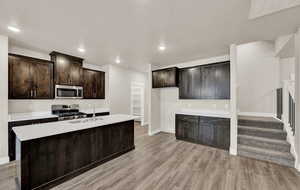 Kitchen with dark brown cabinetry, stainless steel appliances, light wood finished floors, recessed lighting, and a kitchen island with sink