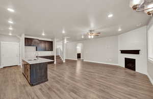 Kitchen with a large fireplace, dark brown cabinets, light wood finished floors, open floor plan, and recessed lighting