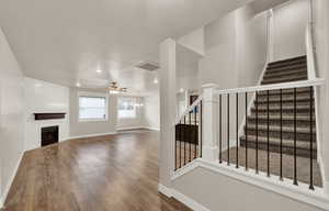 Unfurnished living room with stairway, a large fireplace, wood finished floors, a textured ceiling, and a ceiling fan