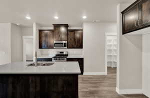 Kitchen with dark brown cabinets, appliances with stainless steel finishes, light stone counters, recessed lighting, and a kitchen island with sink