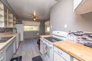 Kitchen with white range with electric stovetop, backsplash, open shelves, light wood-style floors, and ceiling fan