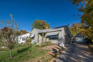 Bungalow featuring an outbuilding, a detached garage, a chimney, asphalt driveway, and a front lawn