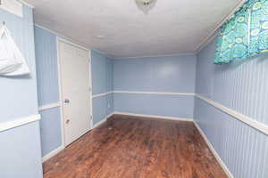 Empty room with dark wood-style flooring, a textured ceiling, and wood walls
