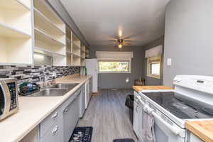 Kitchen with white electric range oven, open shelves, light wood-style flooring, stainless steel microwave, and decorative backsplash