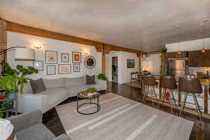 Living room with dark hardwood floors, beamed ceiling, and a brick wall