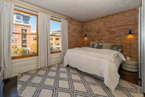 Bedroom with brick walls, large Pella windows, a textured wall, and wood floors