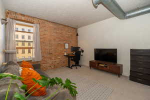 Carpeted 2nd bedroom with a brick wall, east facing window, and extra storage above closet