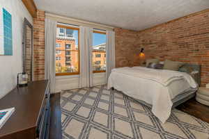 Bedroom with brick walls, large Pella windows, a textured wall, and wood floors