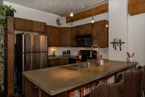 Kitchen with concrete countertops, stainless steel appliances, dark brown wooden cabinets, pendant lighting, and a peninsula with illuminated storage