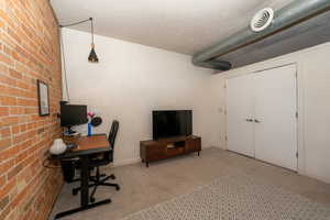 Carpeted 2nd bedroom with a brick wall, east facing window, and extra storage above closet