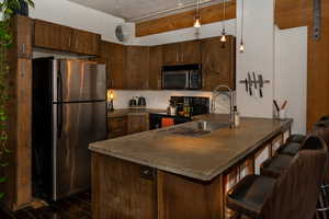 Kitchen with concrete countertops, stainless steel appliances, dark brown wooden cabinets, pendant lighting, and a peninsula with illuminated storage