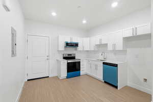 Entrance opens into kitchen with white cabinetry, light countertops, electric stove, dishwashing machine, and light wood finished floors