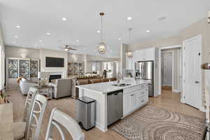 Kitchen with white cabinets, appliances with stainless steel finishes, pendant lighting, open floor plan, and light wood-style flooring