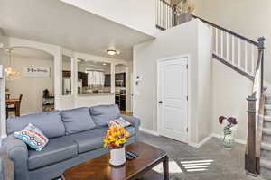 Living room with a chandelier, stairs, arched walkways, carpet floors, and a towering ceiling