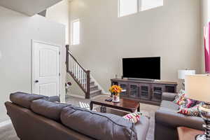 Living area with carpet, plenty of natural light, a towering ceiling, and stairs
